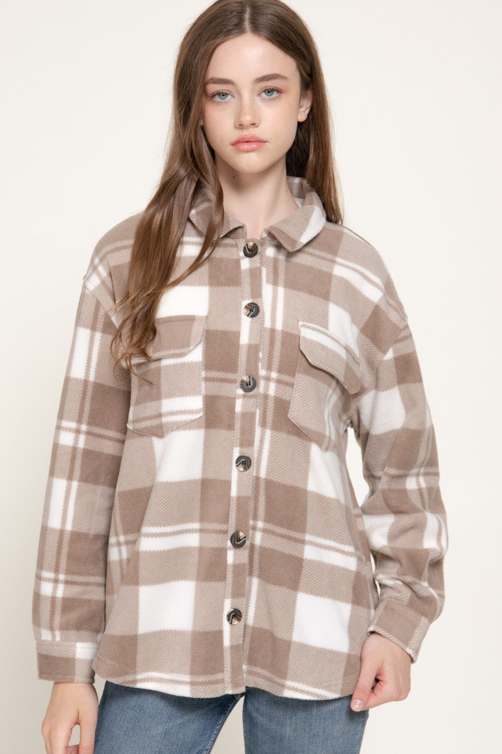Model wearing an oversized taupe and cream plaid shacket with button closure and two chest pockets, paired with blue jeans.