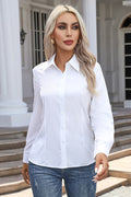 A woman with blonde hair wearing a white long-sleeve button-up shirt and blue jeans, standing in front of a white building with columns and steps.
