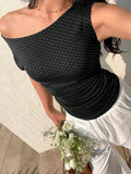 Woman wearing a black off-shoulder dress with white polka dots, holding flowers against a light background.