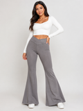 A woman modeling a two-piece outfit consisting of a white long-sleeve crop top and high-waisted, wide-leg gray pants, standing against a light gray studio background.