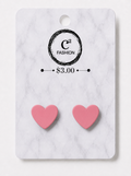 A pair of pink heart-shaped stud earrings displayed on a white marble-patterned retail card with the brand name C² FASHION and a $3.00 price printed on it.