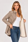 A woman models a taupe-brown corduroy button-up shirt jacket with a cream sherpa lining, worn open over a white tank top and blue jeans, against a light gray studio background.