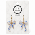 A pair of dangling bow earrings with blue and white floral enamel detailing and gold-tone hooks, displayed on a white marble-style retail card with the brand name C² FASHION and a price of $5.00.