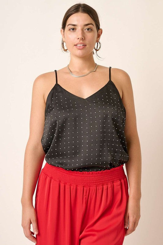 Woman wearing a black polka dot top and red pants against a beige background
