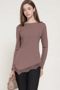 Model wearing a mauve long-sleeve ribbed top with an asymmetrical lace-trimmed hem, paired with black pants.
