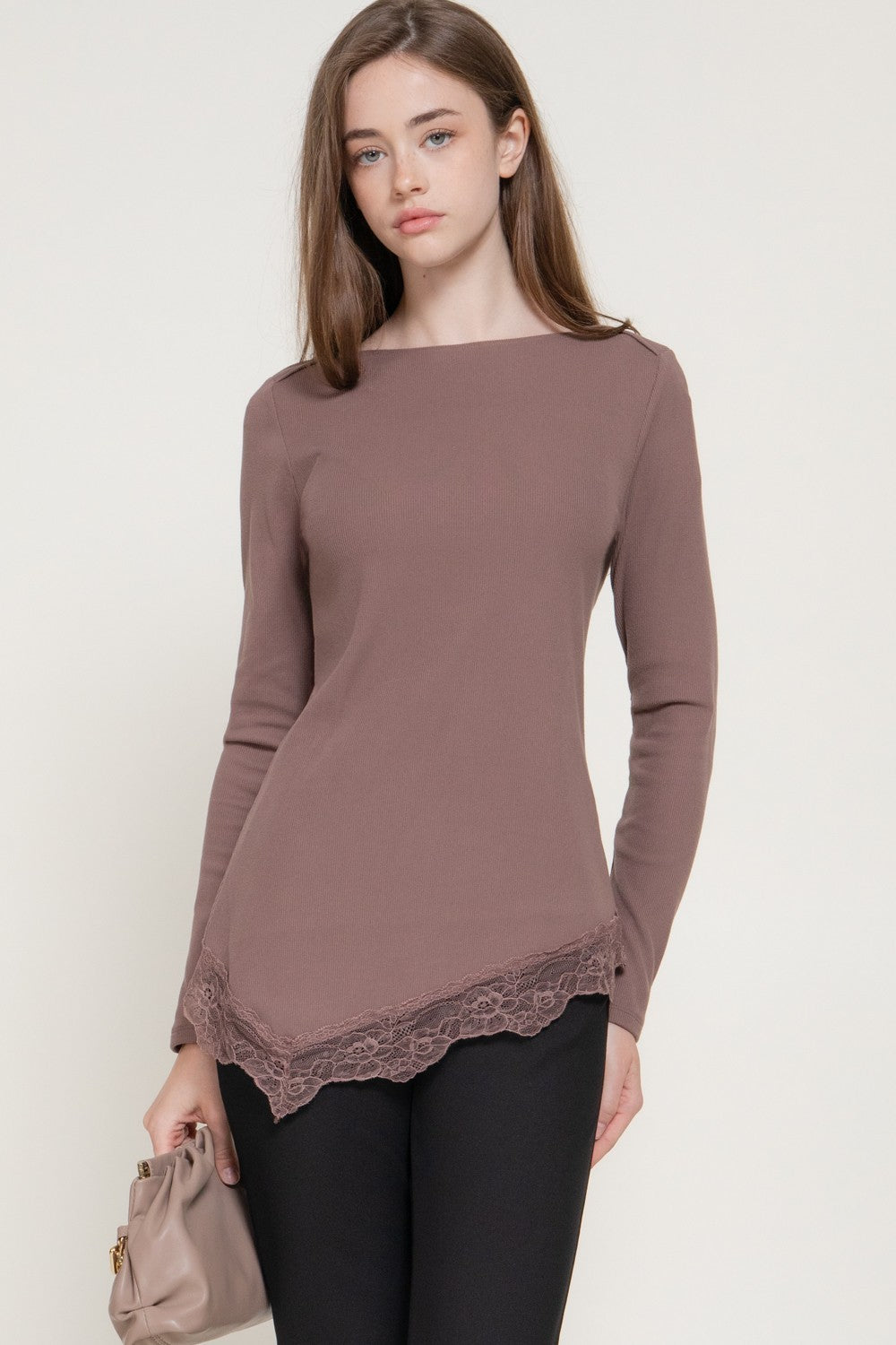 Model wearing a mauve long-sleeve ribbed top with an asymmetrical lace-trimmed hem, paired with black pants.