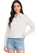 A woman modeling a white long-sleeve button-up blouse with black polka dots, paired with light blue denim shorts, against a plain white background.