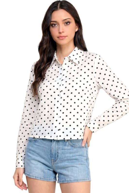 A woman modeling a white long-sleeve button-up blouse with black polka dots, paired with light blue denim shorts, against a plain white background.