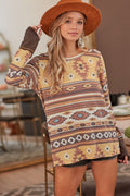 A woman wearing a long-sleeve bohemian-style patterned tunic top in beige, brown, and rust tones, paired with a wide-brimmed brown hat and dangling earrings, standing in a softly blurred indoor setting.