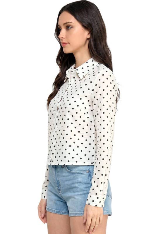 A woman wearing a white long-sleeve button-up blouse with a black polka dot pattern, paired with light blue denim shorts, shown from a side profile against a plain white background.