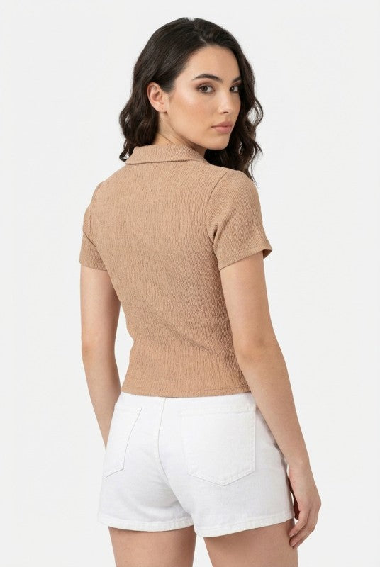 Woman wearing a brown ribbed polo shirt and white shorts on a light gray background