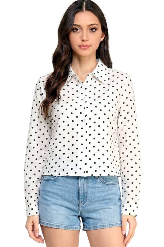 A woman modeling a white long-sleeve button-up blouse with a black polka dot pattern, paired with light blue denim shorts, against a plain white background.