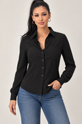 A woman modeling a black long-sleeve button-up blouse with a pointed collar and chest pocket, paired with blue jeans, against a plain light gray studio background.