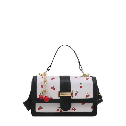 A structured handbag with a white body covered in a red cherry print, black leather trim and handle, and gold-tone hardware including a decorative cherry charm.