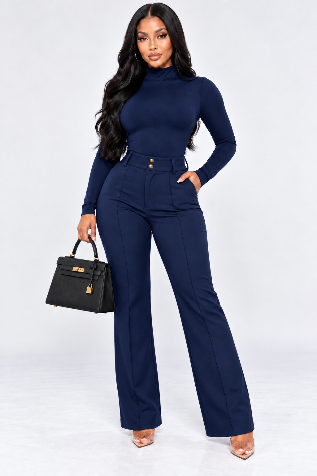 A woman modeling a navy blue long-sleeve mock-neck top and matching high-waisted wide-leg trousers, holding a black handbag with gold hardware against a light gray studio background.