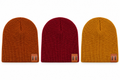 Three ribbed knit beanie hats shown side by side on a plain white background, in rust orange, deep red, and mustard yellow, each with a small tan leather patch near the lower edge.