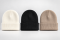 Three ribbed knit beanie hats in off-white, black, and light beige, arranged side by side against a light gray background.