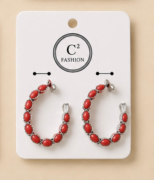 Silver-tone hoop earrings featuring vibrant oval red stones, displayed on a white C² Fashion jewelry card.