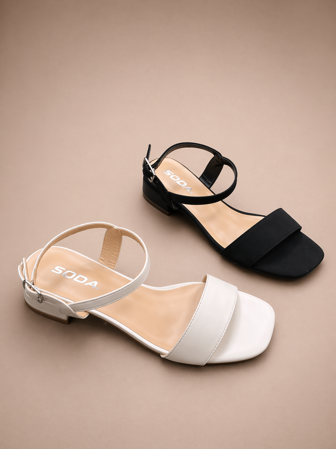 Black and white sandals with 'SODA' branding on a beige background