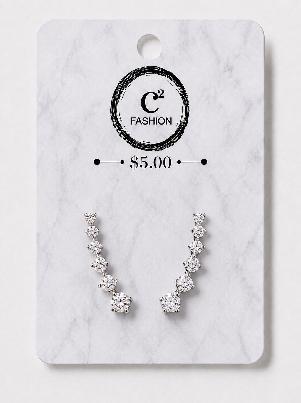 A pair of silver-toned crescent-shaped stud earrings with clear gemstones, displayed on a white marble-style card with the brand name C2 FASHION and a $5.00 price printed on it.