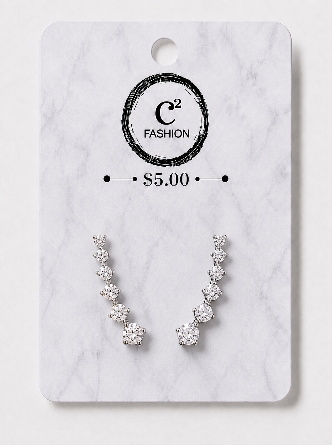 A pair of silver-toned crescent-shaped stud earrings with clear gemstones, displayed on a white marble-style card with the brand name C2 FASHION and a $5.00 price printed on it.