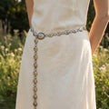 Person wearing a white dress with an ornate belt in a natural setting