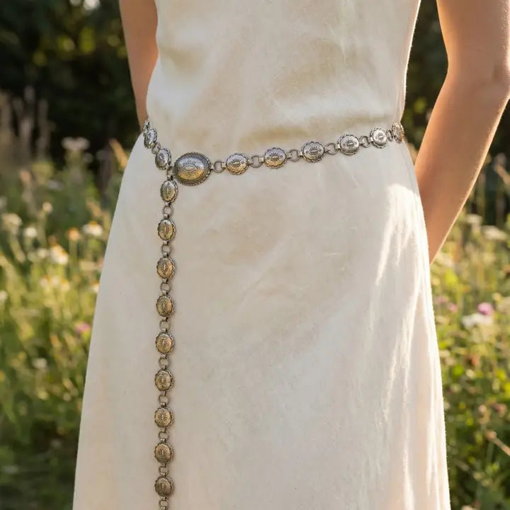 Person wearing a white dress with an ornate belt in a natural setting