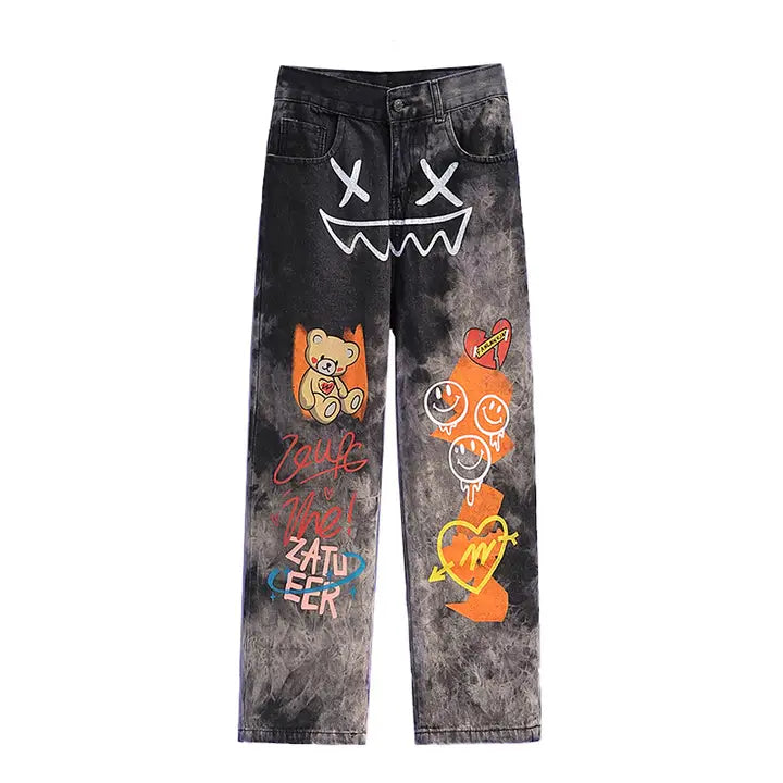 Black acid wash jeans with colorful graffiti designs including smiley face, teddy bear, and street art graphics on front legs.