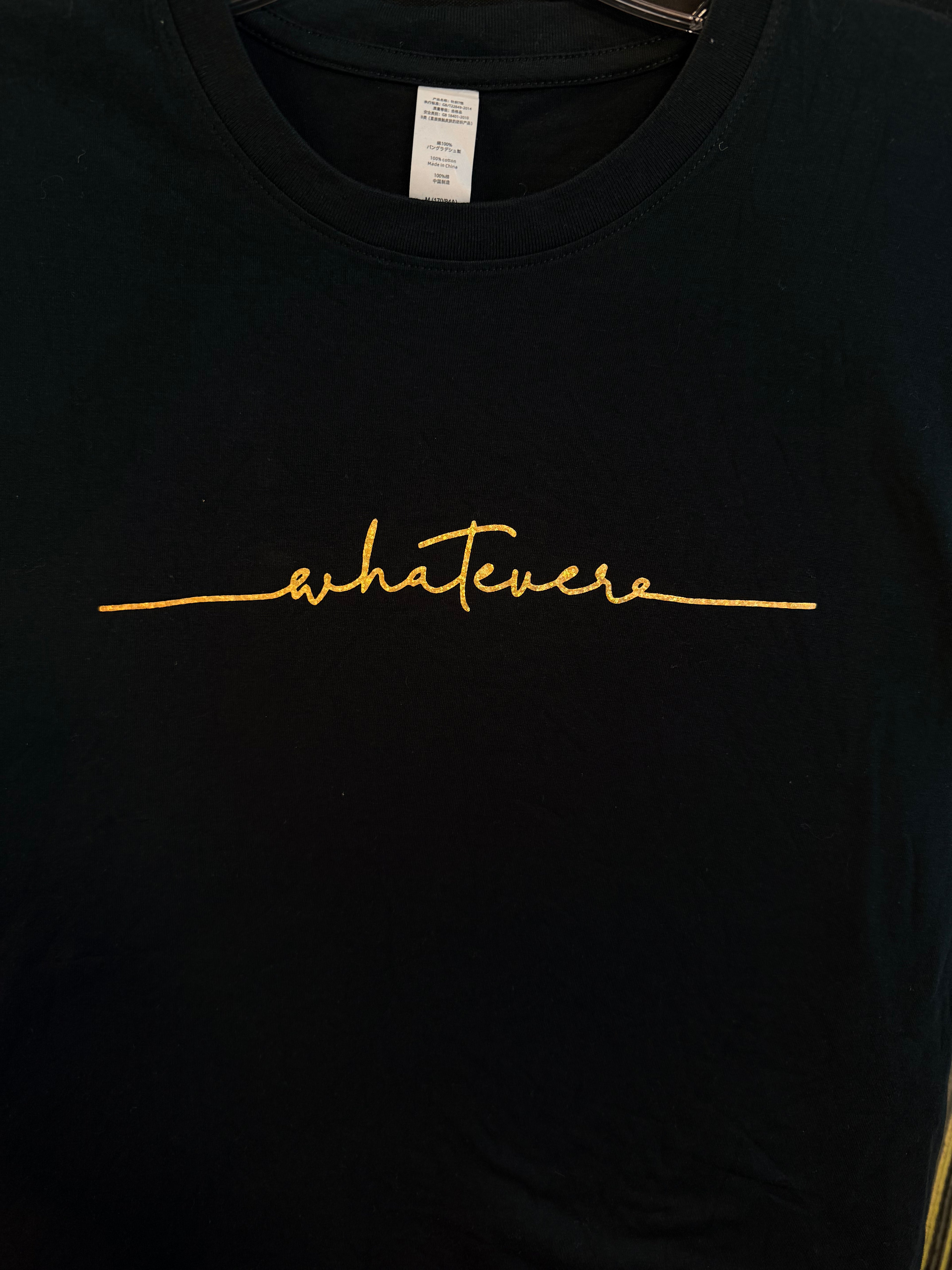 Black t-shirt with gold 'whatevs' text on a plain background