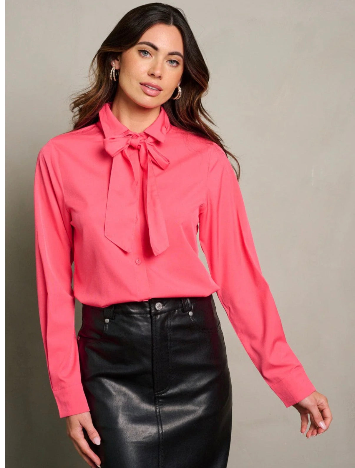 Woman wearing a pink blouse with a tie neckline and black leather skirt on a neutral background