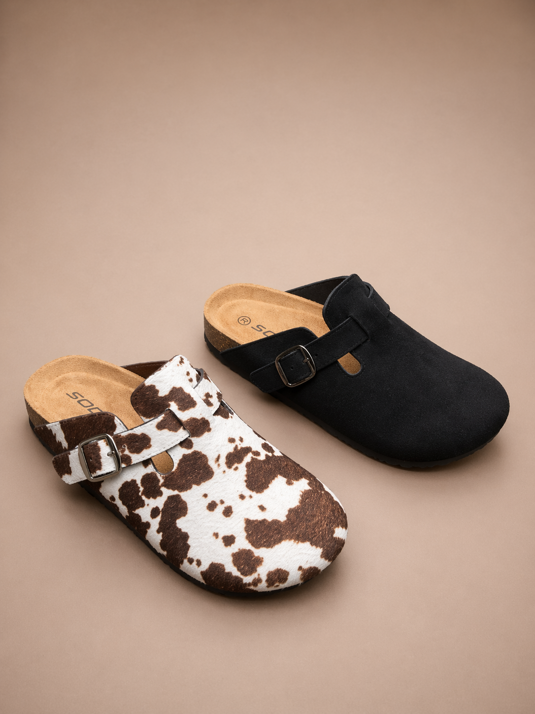 Two clogs, one with a cow print and the other black, on a beige background.