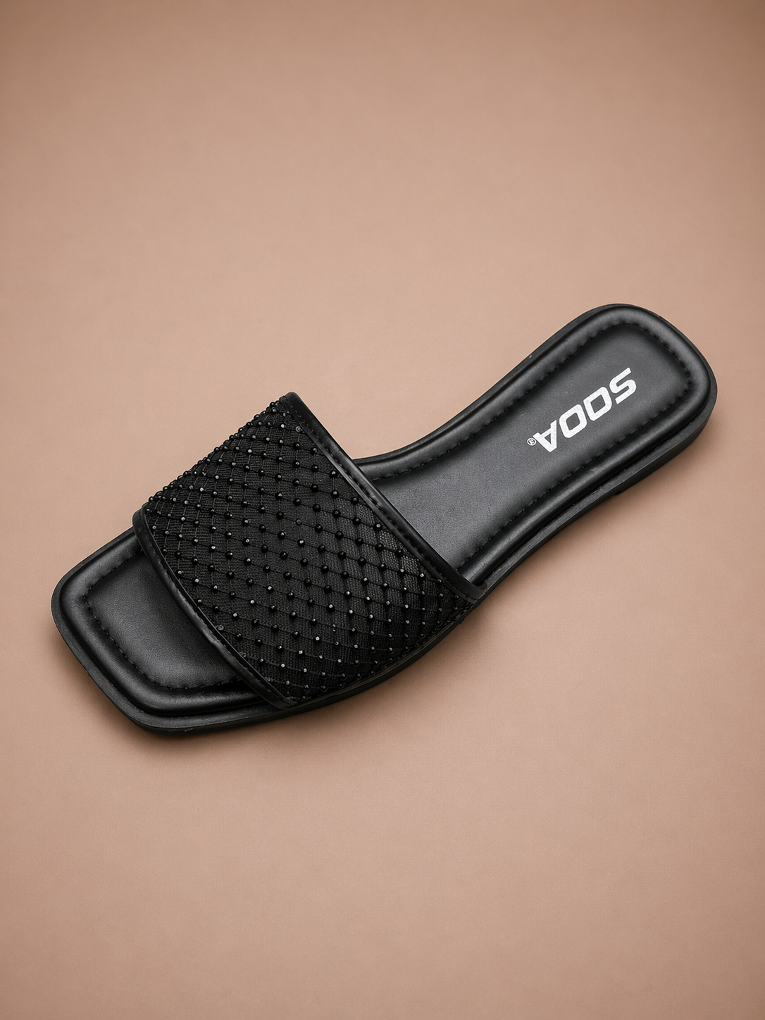 Black slide sandal with rhinestone details on a beige background