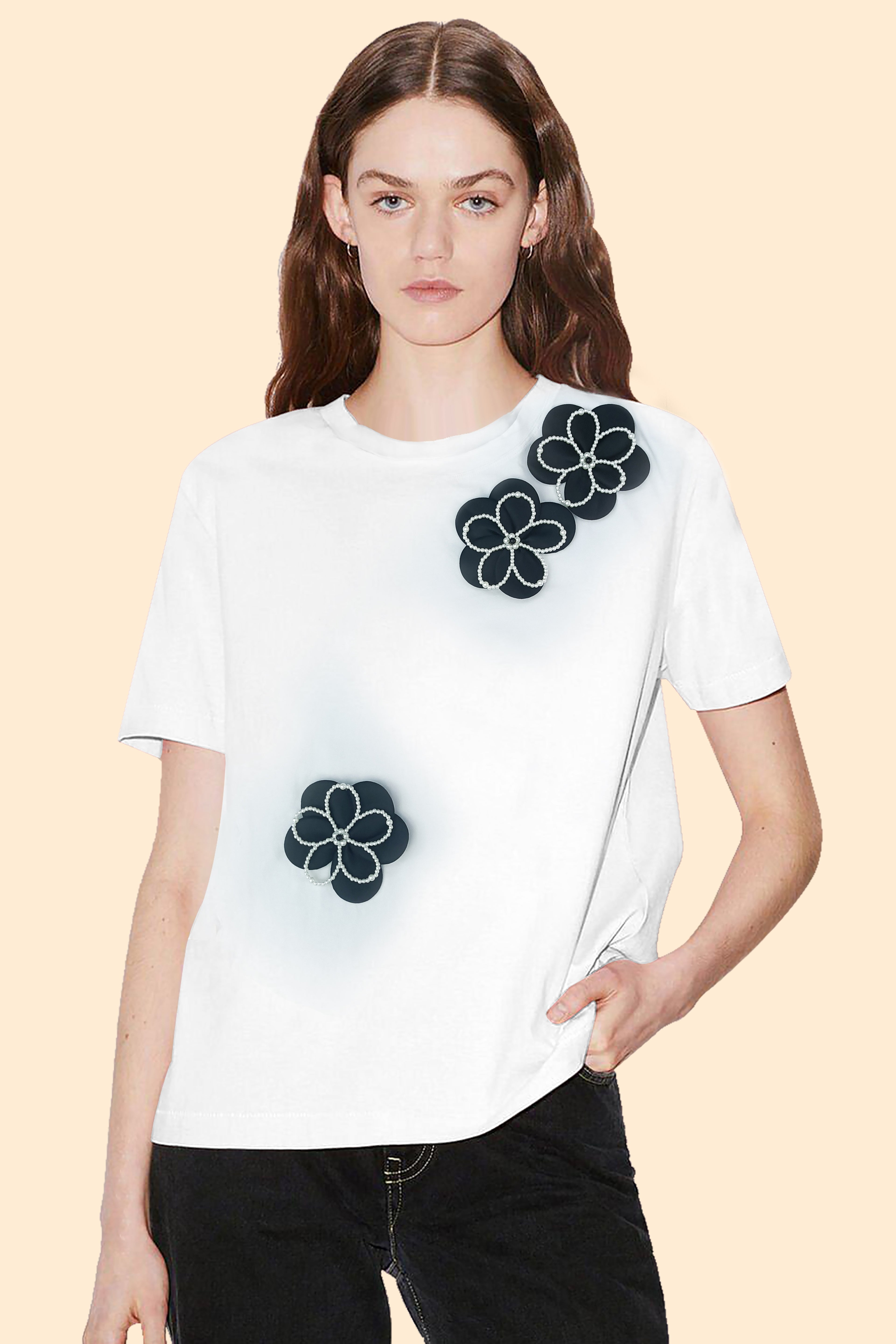 Model wearing a white short-sleeve tee with white floral appliqué details, styled with dark denim for a casual chic look.