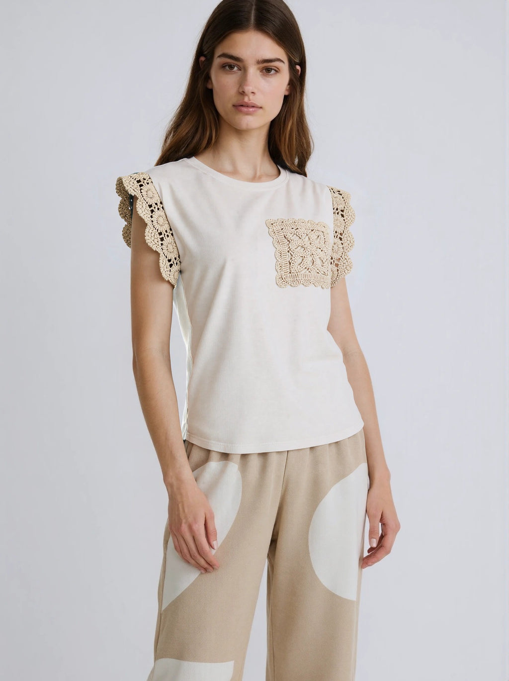 Woman wearing a white top with lace details on a plain background
