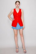 A woman modeling a bright red sleeveless vest with a V-neck and front buttons, paired with a denim mini skirt and gray heeled sandals, against a light gray studio background.