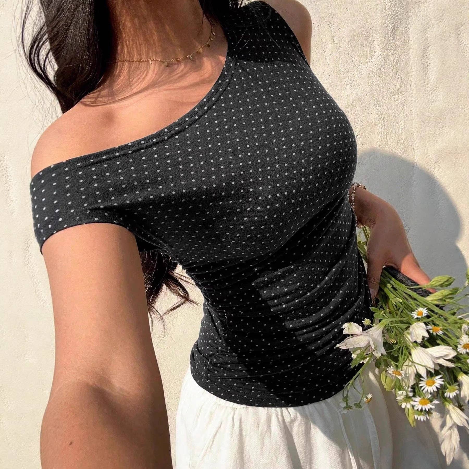 Woman wearing a black polka dot top holding flowers against a light background