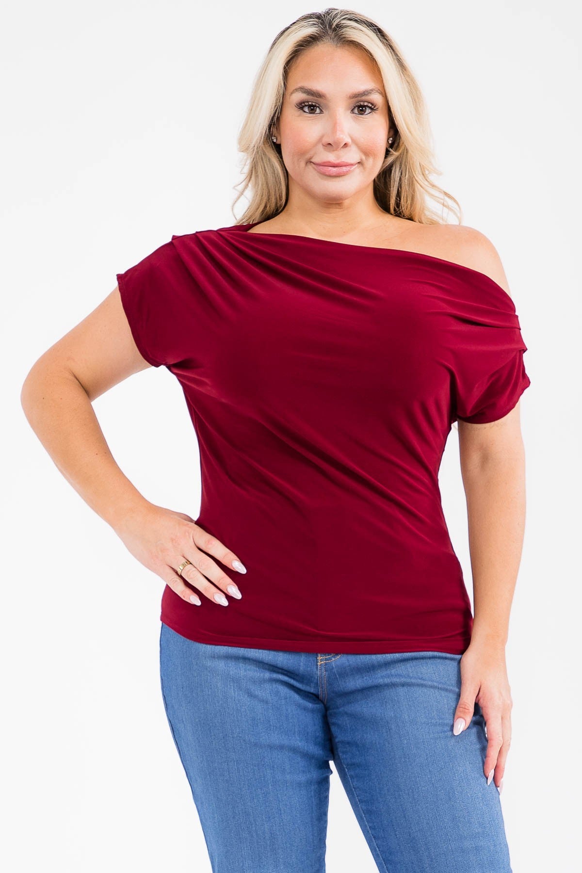 A woman modeling a burgundy off-the-shoulder short-sleeve top with blue jeans, photographed against a plain white studio background.