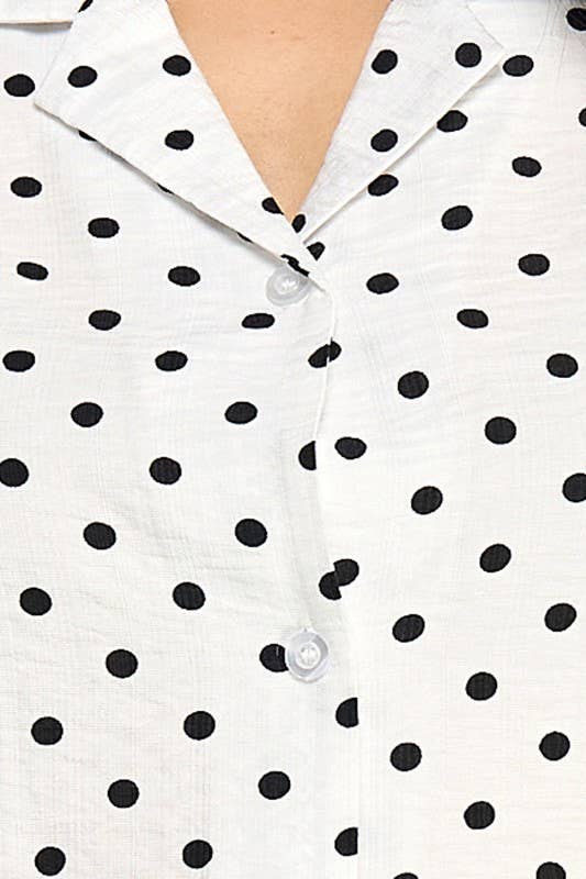 Close-up of a white button-front shirt with black polka dots and a pointed collar, worn by a model.