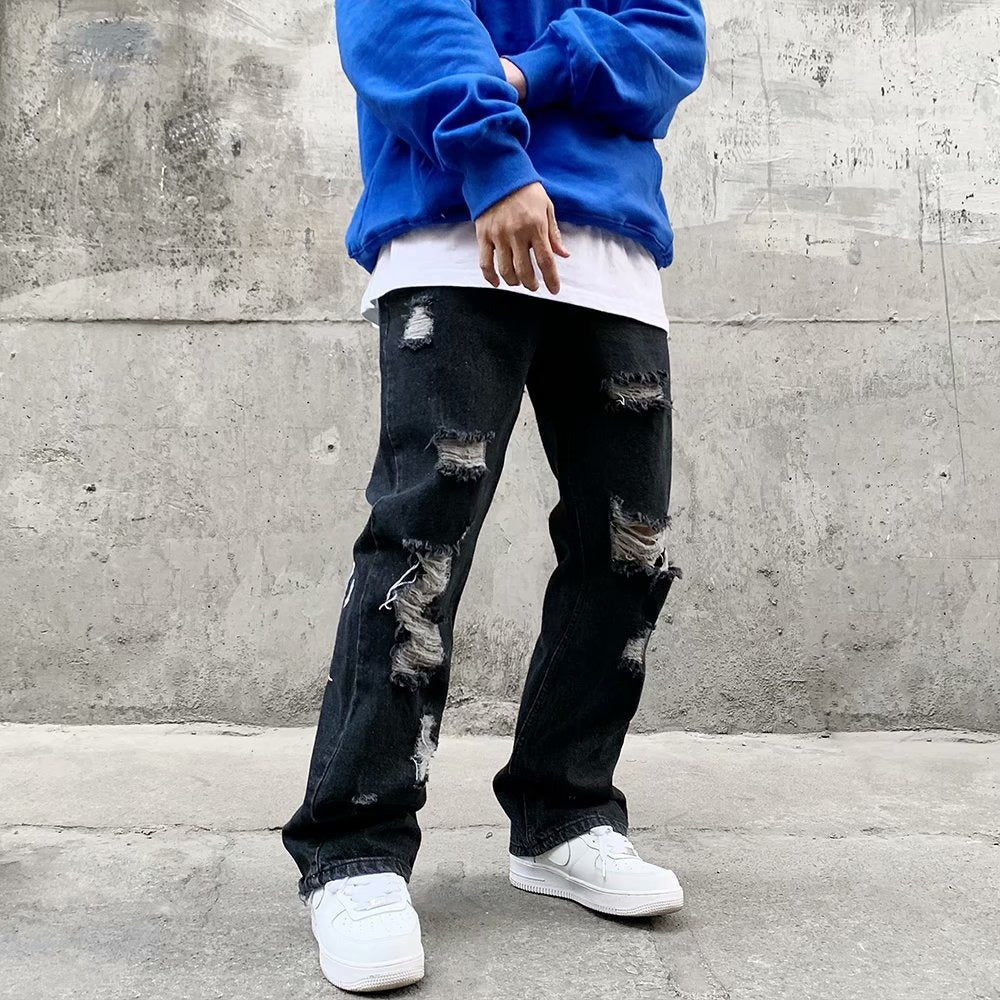 Black distressed jeans with ripped details on the front and bold white gothic lettering printed down the back legs.