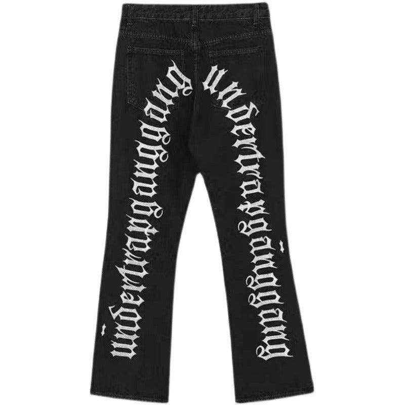 Black distressed jeans with ripped details on the front and bold white gothic lettering printed down the back legs.
